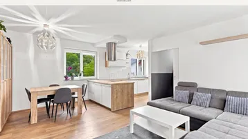 Heller offener Wohn-Essbereich mit moderner Küche, Holzboden und gemütlichem Sofa.