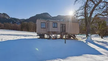 Modernes Tiny House aus Holz auf Rädern in einer verschneiten Landschaft mit Bergblick.