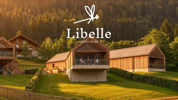 Moderne Chalets in alpiner Landschaft mit Wald und Bergen im Hintergrund bei Sonnenuntergang.