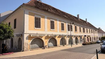 Historisches Gebäude mit mehreren gewölbten Ladenfronten und Fenstern im Obergeschoss an einer Straße.