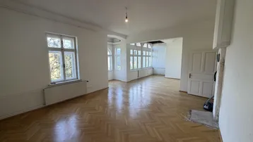 Helles Zimmer mit Fischgrätparkettboden und großen Fenstern, das viel Tageslicht hereinlässt.