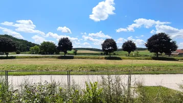 Weitläufige ländliche Landschaft mit Feldern, Bäumen und blauem Himmel, ideal für Naturliebhaber.