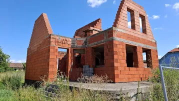 Rohbau eines Einfamilienhauses mit Ziegelmauerwerk und offener Bauweise unter blauem Himmel.