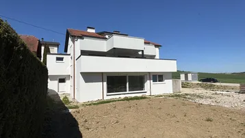 Modernes Wohnhaus mit weißer Fassade und großzügigen Balkonen, umgeben von einer noch unfertigen Gartenfläche.