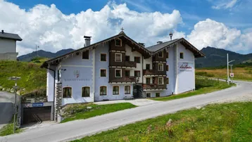 Traditionelles Hotelgebäude in den Bergen mit Balkonen und einer Tiefgarageneinfahrt.