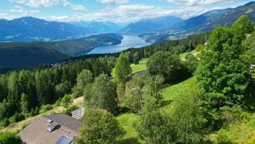 Luftaufnahme eines Hauses mit Solarpaneelen, umgeben von grüner Natur, See und Bergen.