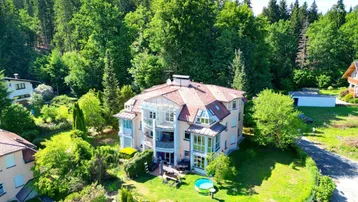 Luftaufnahme eines Mehrfamilienhauses umgeben von viel Grün und Wald.