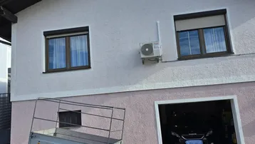 Vorderansicht eines Wohnhauses mit Garage, Fenstern und einer Klimaanlage an der Fassade.