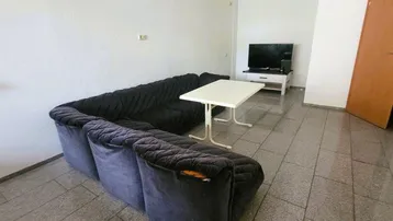 Geräumiges Wohnzimmer mit großem Sofa, Fliesenboden und schlichten weißen Wänden.