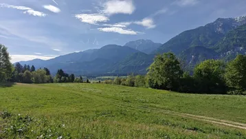 Weitläufige grüne Wiesenlandschaft mit majestätischen Bergen im Hintergrund unter blauem Himmel.