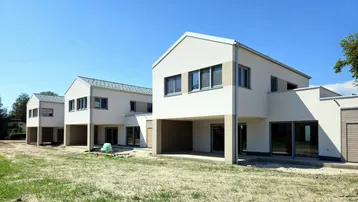 Moderne Neubauten mit heller Fassade und Satteldach unter blauem Himmel, umgeben von unbebautem Land.