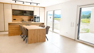 Heller offener Wohn- und Essbereich mit moderner Küche, Holzelementen und Zugang zur Terrasse.