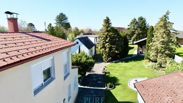 Luftaufnahme eines Hauses mit großem Garten und umliegenden Bäumen unter blauem Himmel.