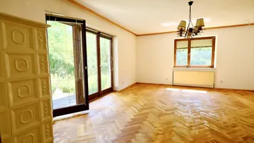 Helles Wohnzimmer mit traditionellem Kachelofen, Fischgrätparkett und Zugang zur Terrasse mit Grünblick.
