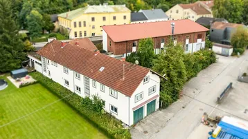 Luftaufnahme des Anwesens mit Hauptgebäude, Nebengebäude und umliegender Grünfläche, umgeben von weiteren Häusern.