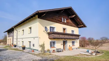 Traditionelles Landhaus mit gelber Fassade, Holzbalkon und Satteldach in ländlicher Umgebung.