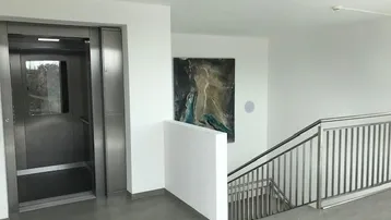 Heller Flur mit modernem Aufzug und Treppenhaus, ausgestattet mit einem Kunstwerk.
