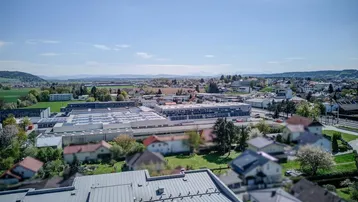 Luftaufnahme der Stadt mit Industriegebiet, Wohnsiedlungen und Bergen im Hintergrund.