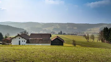 Weitläufige Landschaft mit mehreren Häusern und grünen Feldern unter einem blauen Himmel.