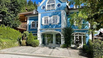 Historisches Gebäude mit leuchtend blauer Fassade, weißen Fensterläden und einem eleganten Eingangsbereich.