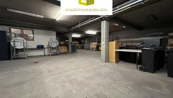 Großer, offener Lagerraum mit Betonboden und sichtbaren Deckenbalken, ideal für gewerbliche Nutzung.