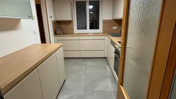 Moderne Küche mit hellen Schränken, Holz-Arbeitsplatten und grauen Fliesenböden.