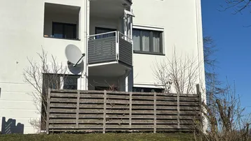 Außenansicht eines Wohngebäudes mit mehreren Balkonen und einem Holzzaun im Vordergrund.