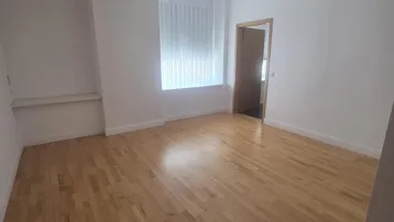 Helles Zimmer mit Holzboden, weißen Wänden und einem Fenster mit Jalousien.