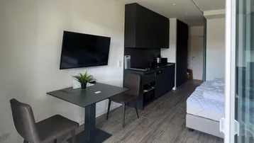 Moderner Studio-Apartment-Bereich mit integrierter Küchenzeile, Esstisch und Schlafbereich.