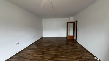 Geräumiges Zimmer mit Laminatboden und weißen Wänden, bereit zur individuellen Gestaltung.