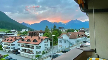 Blick vom Balkon auf die umliegende Berglandschaft und die Dächer der Häuser bei Sonnenuntergang.