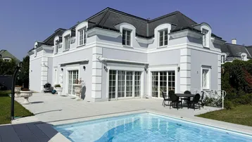Elegantes Haus mit Mansarddach, großem Pool und gepflasterter Terrasse für entspannte Stunden im Freien.
