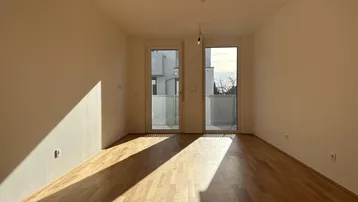 Helles, leeres Zimmer mit Parkettboden und Zugang zu einem französischen Balkon.