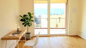 Heller Arbeitsbereich mit Holzboden, modernem Schreibtisch und Zugang zu einem Balkon mit Bergblick.