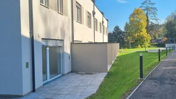 Neubau-Reihenhaus mit kleiner Terrasse und Rasenfläche im Freien unter blauem Himmel.