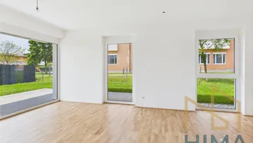 Geräumiges, unmöbliertes Wohnzimmer mit hellem Holzboden und Blick ins Grüne.