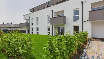 Modernes Mehrfamilienhaus mit weißer Fassade, Balkonen und gepflegter Grünfläche.