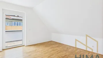 Leeres Schlafzimmer im Dachgeschoss mit Holzboden und Zugang zu einem französischen Balkon.