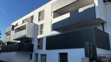 Moderne Wohnanlage mit weißer Fassade und grauen Balkonen unter blauem Himmel.