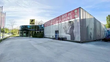 Außenansicht eines großen Geschäftsgebäudes mit Werbebanner und Parkplatz unter blauem Himmel.