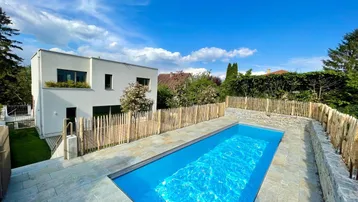 Modernes Haus mit privatem Pool und gepflegtem Garten unter blauem Himmel.