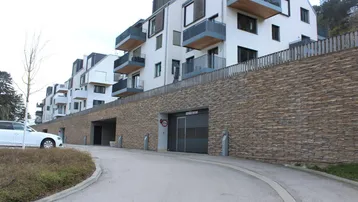 Moderne Wohnanlage mit weißen Fassaden, Balkonen und einer Tiefgaragenzufahrt aus Naturstein.