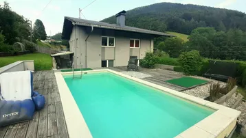 Haus mit Swimmingpool, Holzterrasse und Bergblick in grüner Umgebung, ideal für Entspannung.