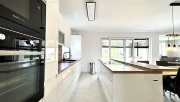Moderne weiße Küche mit integrierten Geräten, Kochinsel und Fliesenboden.