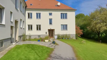 Ansicht des Hauses mit heller Fassade, rotem Ziegeldach und gepflegtem Vorgarten mit Zugangsweg.
