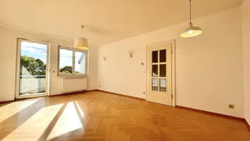 Helles Wohnzimmer mit Fischgrätparkett und Zugang zum Balkon, durchflutet von Sonnenlicht.
