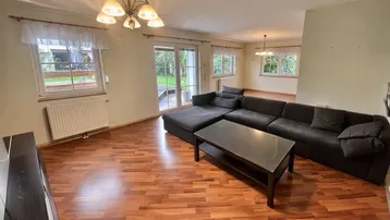 Helles Wohnzimmer mit Laminatboden, großem Sofa und Zugang zum Gartenbereich.
