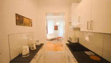 Helle, schmale Küche mit weißen Schränken, dunkler Arbeitsplatte und Blick in den Wohnbereich.