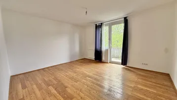 Helles, unmöbliertes Zimmer mit Holzdielenboden und Zugang zu einem Balkon.
