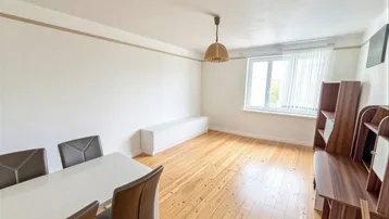 Heller Wohn- und Essbereich mit Holzdielenboden, großem Fenster und schlichten Möbeln.